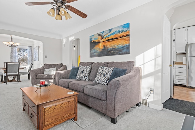 living room featuring arched walkways, light colored carpet, and ceiling fan with notable chandelier