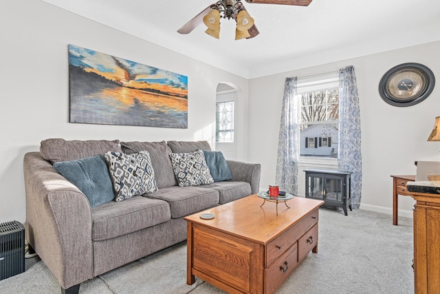 living room featuring light carpet, a ceiling fan, radiator heating unit, arched walkways, and baseboards