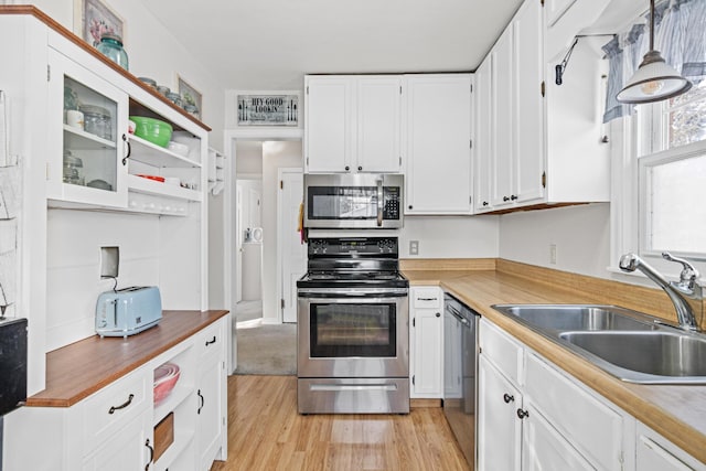 kitchen with a sink, open shelves, appliances with stainless steel finishes, white cabinets, and light wood finished floors