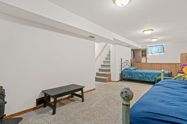 carpeted bedroom with visible vents, baseboards, wood walls, wainscoting, and a textured ceiling