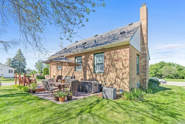 rear view of property featuring a patio, cooling unit, a chimney, a lawn, and brick siding