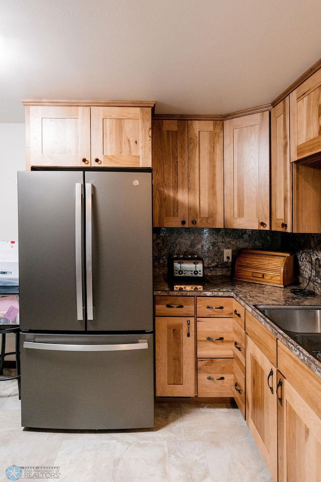 kitchen with light tile flooring, backsplash, stainless steel refrigerator, and dark stone countertops