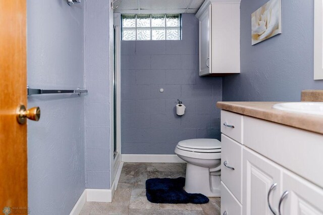 bathroom featuring concrete block wall, vanity, toilet, a shower with door, and baseboards