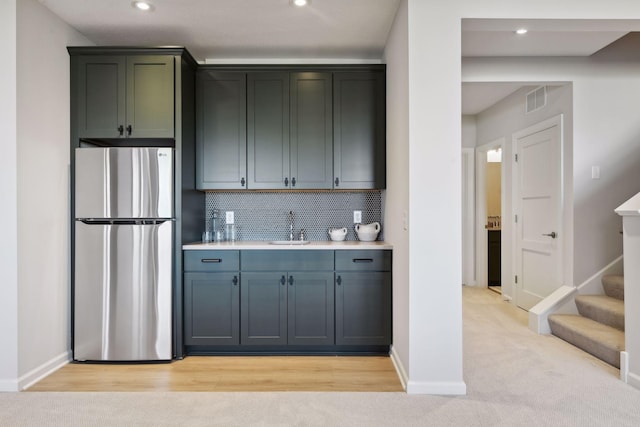 kitchen with light hardwood / wood-style floors, stainless steel fridge, sink, and backsplash