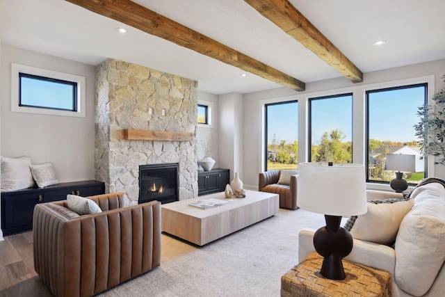 living room with light hardwood / wood-style floors, a stone fireplace, and beam ceiling