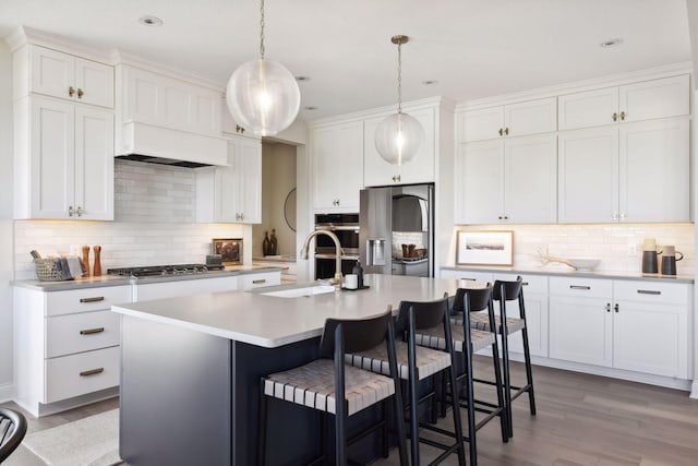 kitchen featuring white cabinets, an island with sink, appliances with stainless steel finishes, light hardwood / wood-style flooring, and pendant lighting