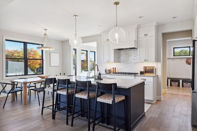 kitchen featuring hardwood / wood-style flooring, hanging light fixtures, a center island with sink, and white cabinets