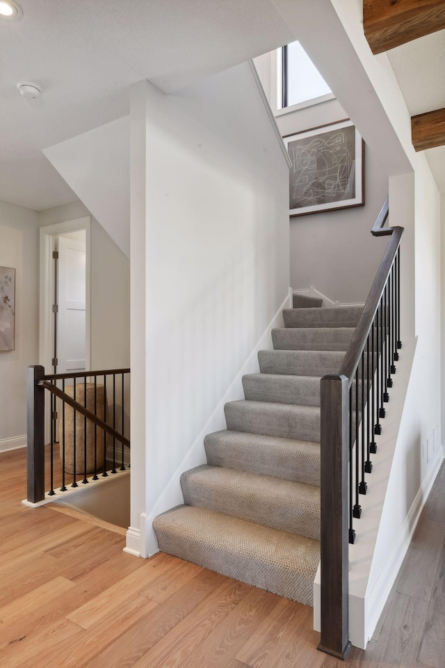 stairs featuring beam ceiling and hardwood / wood-style flooring