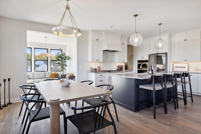 kitchen with hanging light fixtures, light hardwood / wood-style flooring, an island with sink, and white cabinets