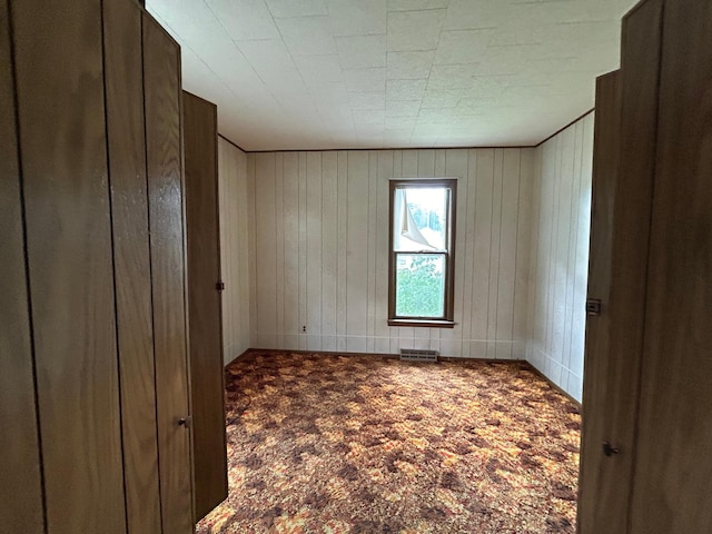 carpeted spare room featuring wood walls