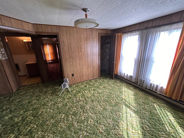 carpeted empty room featuring wooden walls and a baseboard heating unit