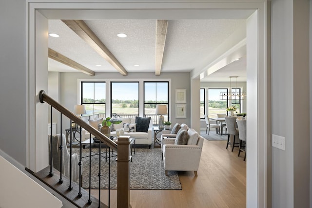 living room featuring a textured ceiling, an inviting chandelier, wood-type flooring, and beam ceiling