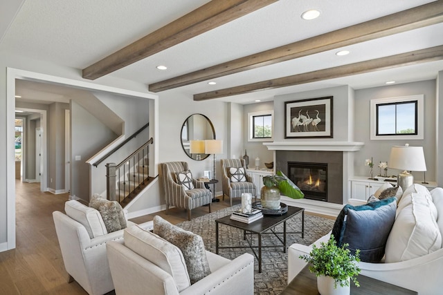 living room with a tiled fireplace, a textured ceiling, wood-type flooring, and beam ceiling