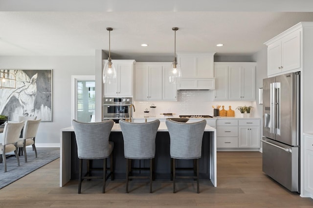 kitchen featuring appliances with stainless steel finishes, tasteful backsplash, wood-type flooring, and an island with sink