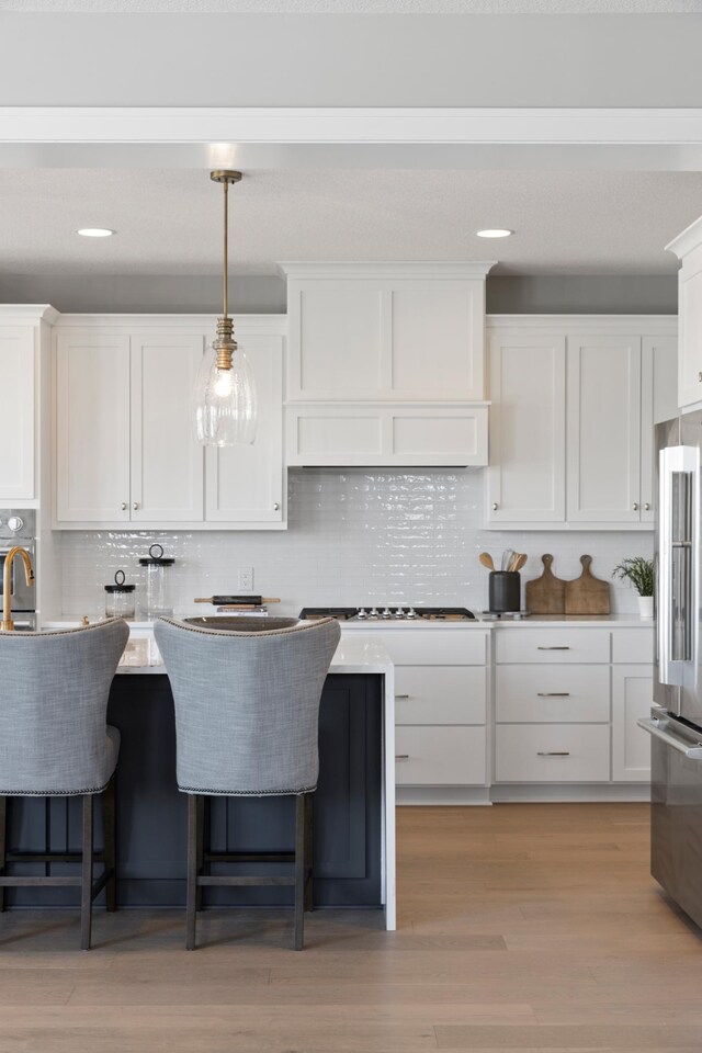 kitchen featuring high end fridge, tasteful backsplash, decorative light fixtures, light wood-type flooring, and white cabinetry