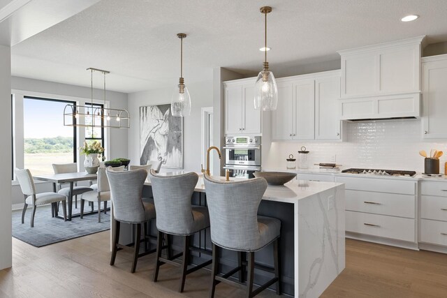 kitchen featuring light hardwood / wood-style flooring, white cabinets, pendant lighting, decorative backsplash, and an island with sink