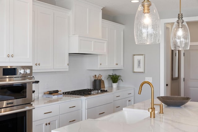 kitchen with white cabinets, light stone countertops, hanging light fixtures, appliances with stainless steel finishes, and decorative backsplash