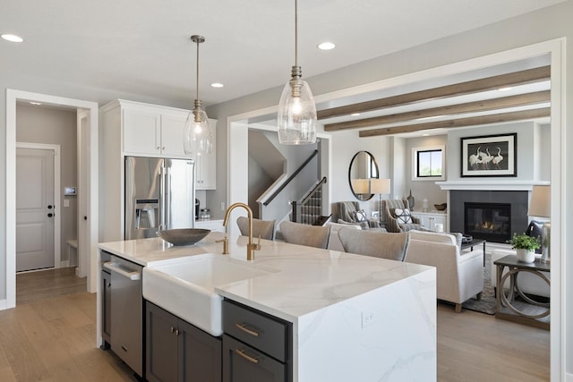 kitchen with light wood-type flooring, white cabinets, an island with sink, hanging light fixtures, and appliances with stainless steel finishes