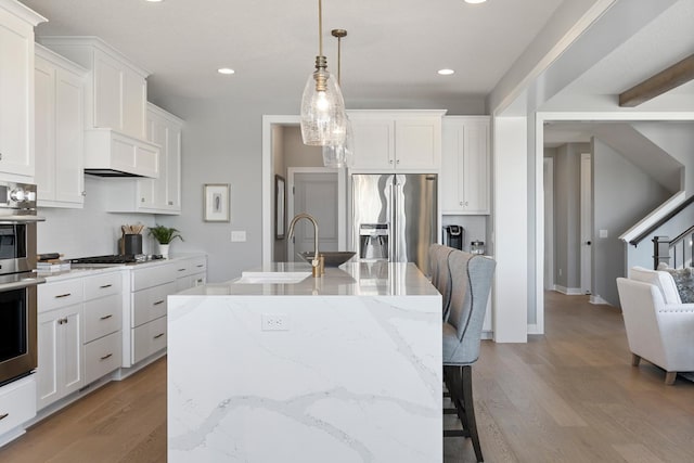 kitchen featuring white cabinetry, stainless steel appliances, hanging light fixtures, a center island with sink, and light hardwood / wood-style flooring