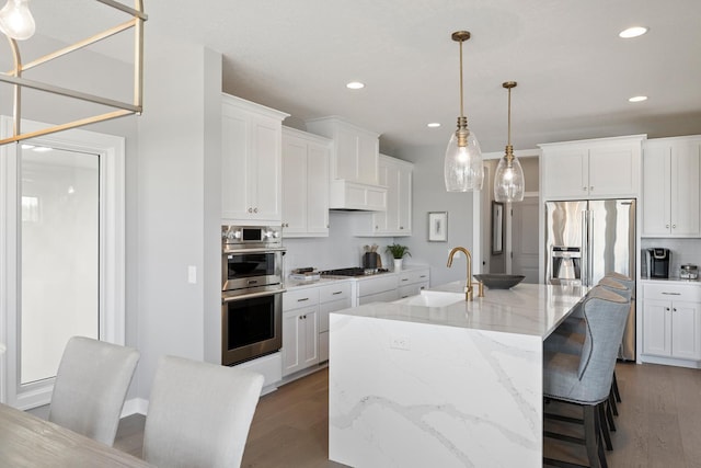 kitchen featuring white cabinets, stainless steel appliances, wood-type flooring, and an island with sink