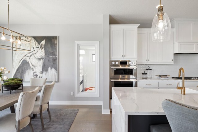 kitchen with decorative light fixtures, stainless steel double oven, light stone counters, and dark wood-type flooring