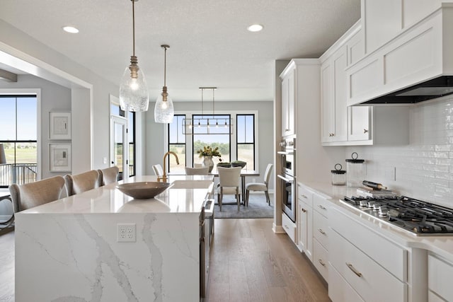 kitchen featuring stainless steel appliances, hardwood / wood-style floors, a center island with sink, backsplash, and custom exhaust hood