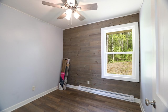 empty room featuring a baseboard radiator, dark wood-type flooring, a ceiling fan, wooden walls, and baseboards