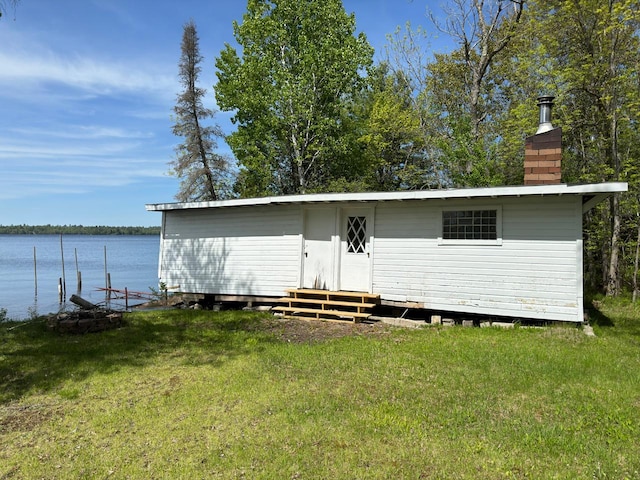 back of house with entry steps, a water view, a lawn, and a chimney