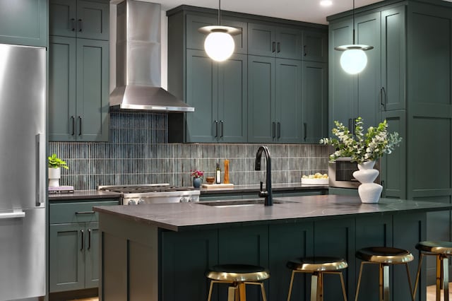 kitchen featuring wall chimney range hood, sink, a kitchen breakfast bar, and stainless steel refrigerator