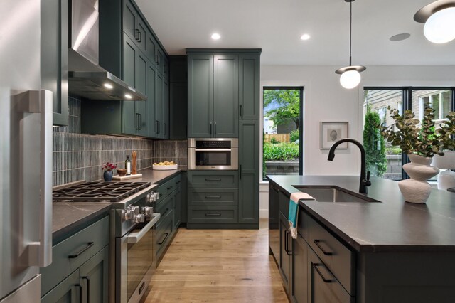 kitchen with wall chimney exhaust hood, sink, decorative light fixtures, stainless steel appliances, and backsplash