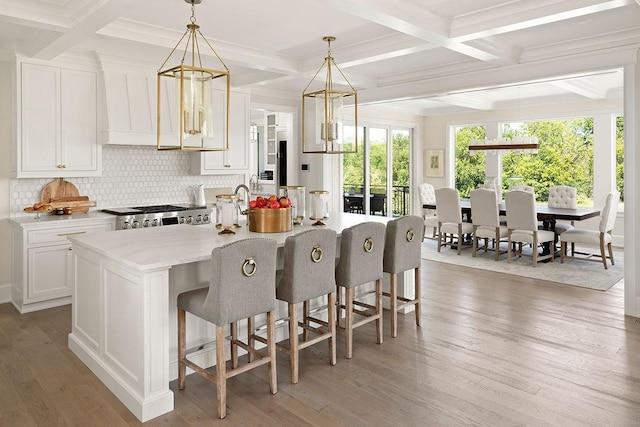 kitchen with hardwood / wood-style flooring, coffered ceiling, a kitchen island with sink, and pendant lighting