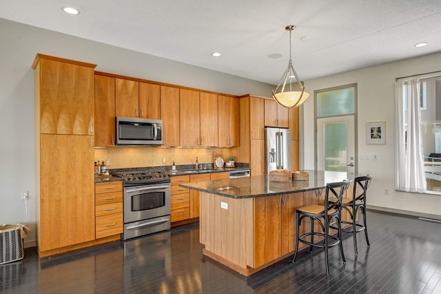 kitchen with decorative light fixtures, a center island, stainless steel appliances, dark hardwood / wood-style floors, and a breakfast bar