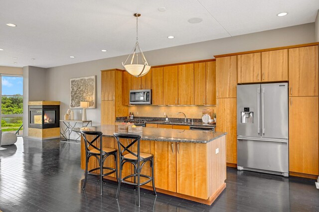 kitchen with appliances with stainless steel finishes, a kitchen breakfast bar, a multi sided fireplace, a kitchen island, and dark hardwood / wood-style flooring