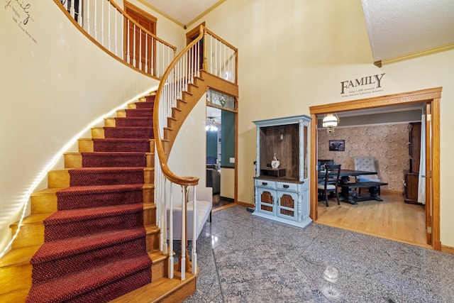 stairway with wood-type flooring, a textured ceiling, a high ceiling, and ornamental molding