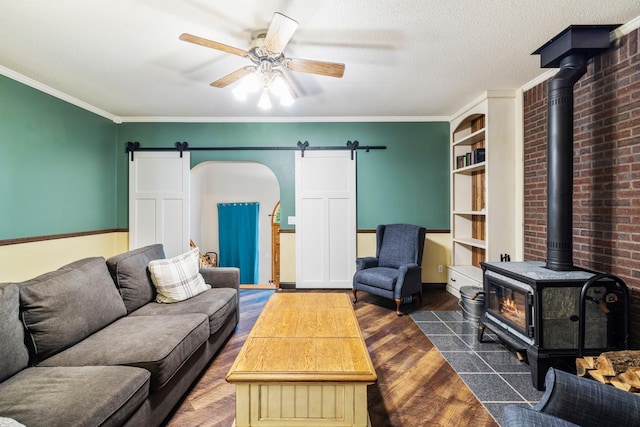 living room with a wood stove, a textured ceiling, a barn door, and ornamental molding