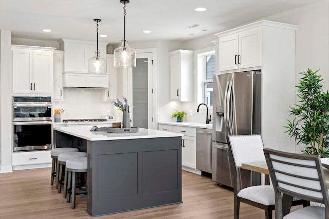 kitchen featuring a center island, hanging light fixtures, light wood-type flooring, appliances with stainless steel finishes, and white cabinetry