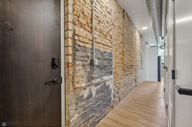 hallway with light hardwood / wood-style floors and brick wall