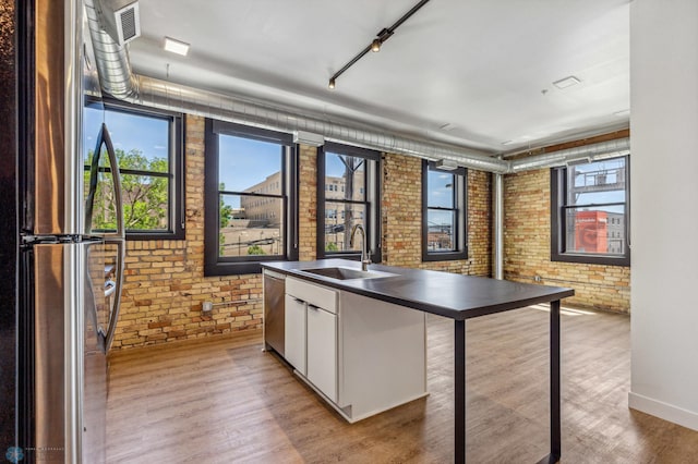 kitchen with white cabinetry, sink, brick wall, and stainless steel appliances