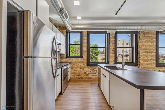 kitchen featuring appliances with stainless steel finishes, brick wall, sink, light hardwood / wood-style flooring, and white cabinetry