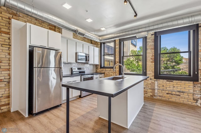 kitchen featuring brick wall, stainless steel appliances, white cabinetry, and sink