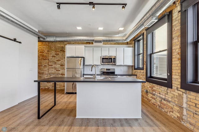 kitchen with light wood-type flooring, white cabinetry, stainless steel appliances, and brick wall