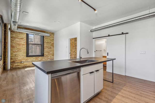 kitchen with light wood-type flooring, stainless steel dishwasher, brick wall, sink, and white cabinets