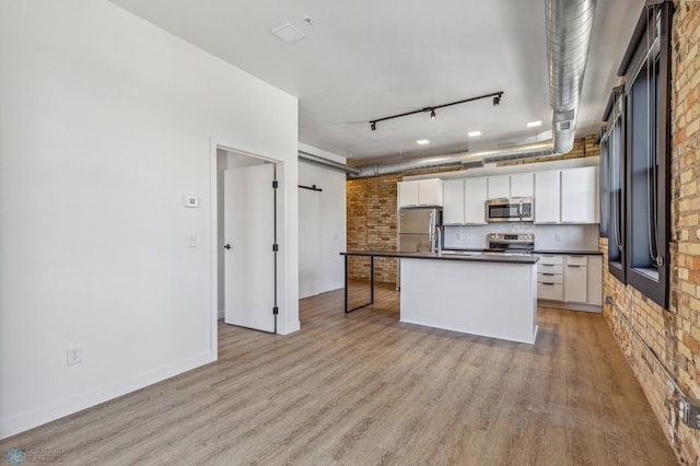 kitchen featuring rail lighting, stainless steel appliances, light hardwood / wood-style flooring, brick wall, and white cabinets