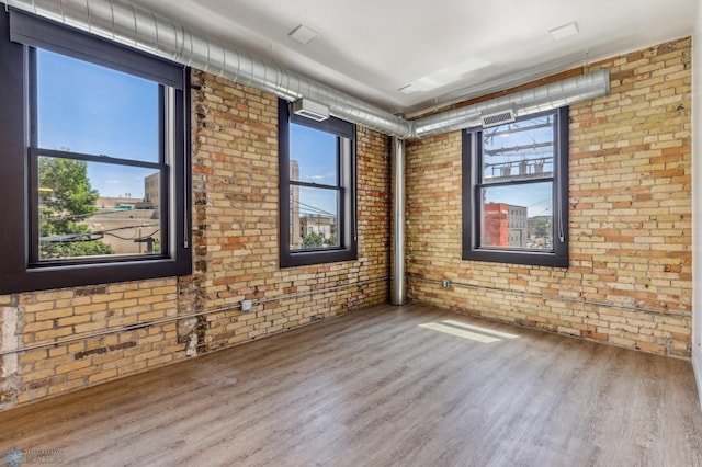 empty room featuring wood-type flooring, a healthy amount of sunlight, and brick wall