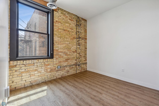 unfurnished room featuring wood-type flooring and brick wall