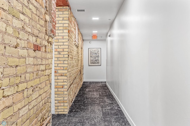 hallway featuring dark carpet and brick wall