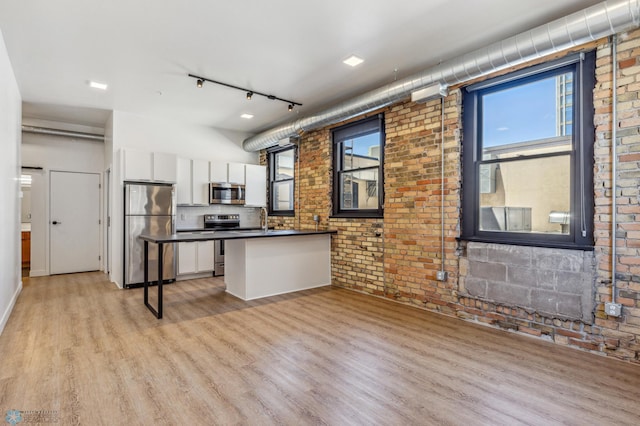 kitchen featuring appliances with stainless steel finishes, brick wall, a breakfast bar, light hardwood / wood-style flooring, and white cabinetry