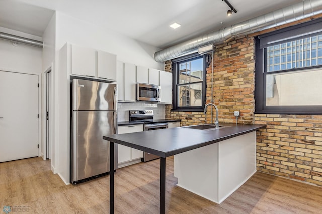 kitchen with appliances with stainless steel finishes, brick wall, sink, light hardwood / wood-style floors, and white cabinetry