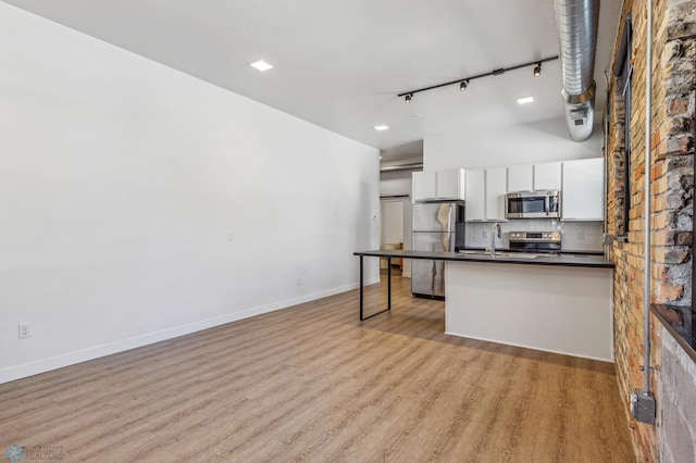 kitchen with decorative backsplash, rail lighting, stainless steel appliances, light hardwood / wood-style flooring, and white cabinetry