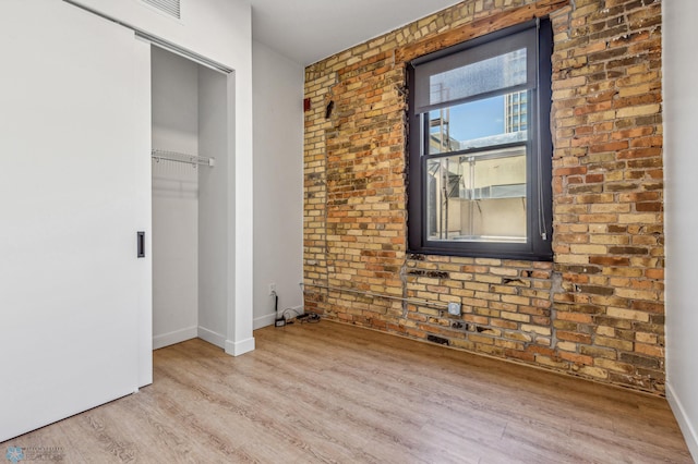 unfurnished bedroom with light hardwood / wood-style floors, a closet, and brick wall